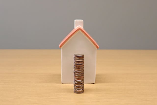 a small house figurine behind a stack of coins